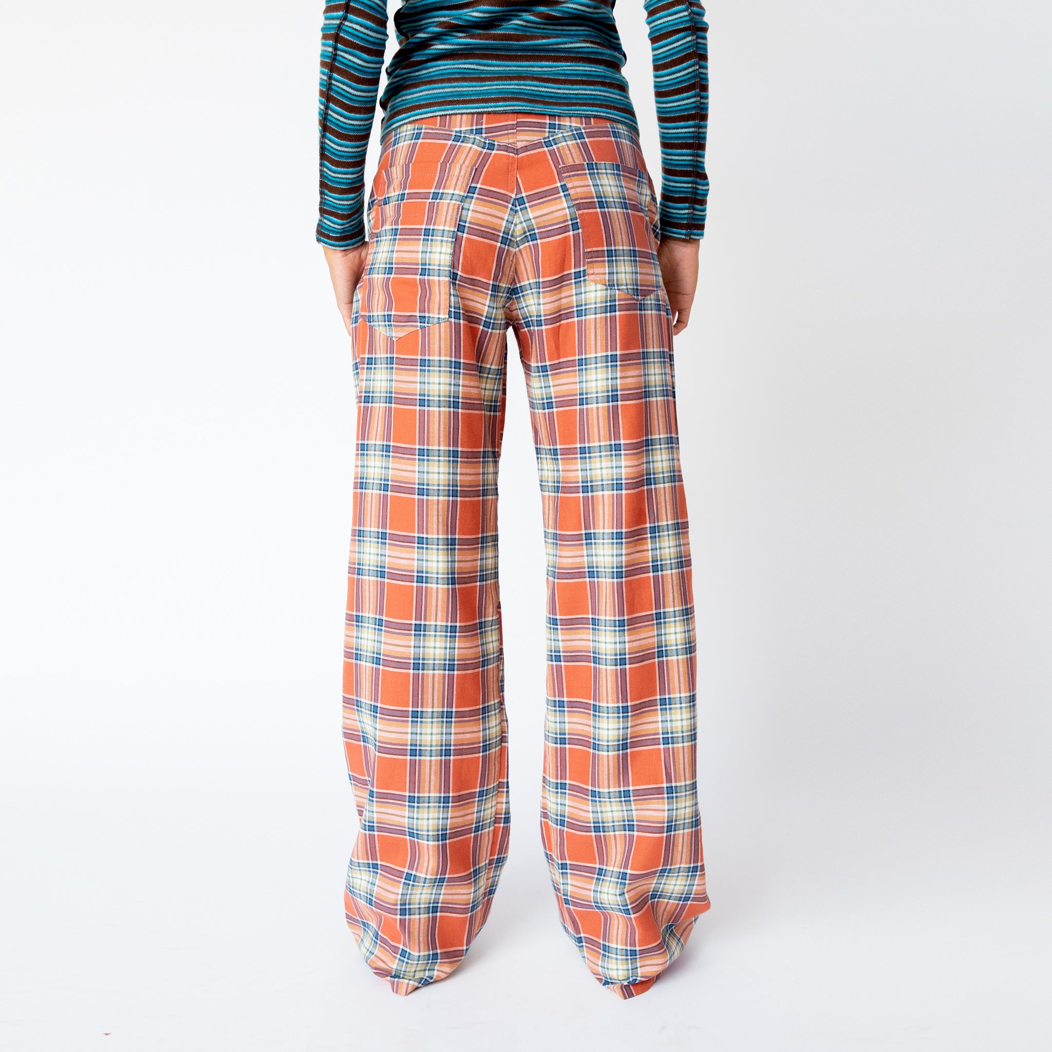 A model wears the coral plaid wide leg Clover Pant by Collina Strada, paired with a blue striped long sleeve - back view.