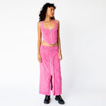 A model looks to the side while wearing the pink corduroy Cord Bustier by Eckhaus Latta, with silver front zipper and wide shoulder straps, paired here with the matching full length corduroy zip skirt.