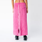 A model wears the full length pink corduroy Cord Zip Skirt by Eckhaus Latta, with full length silver front zipper and 3 front waistband button snaps, paired here with black sneakers - back view.