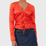 A model wear's GANNI's vibrant red crinkle satin blouse featuring a V neckline and front bodice tied with red satin bows.