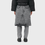 A model wears the acid washed black denim jeans with attached midi skirt with black boots - back view.