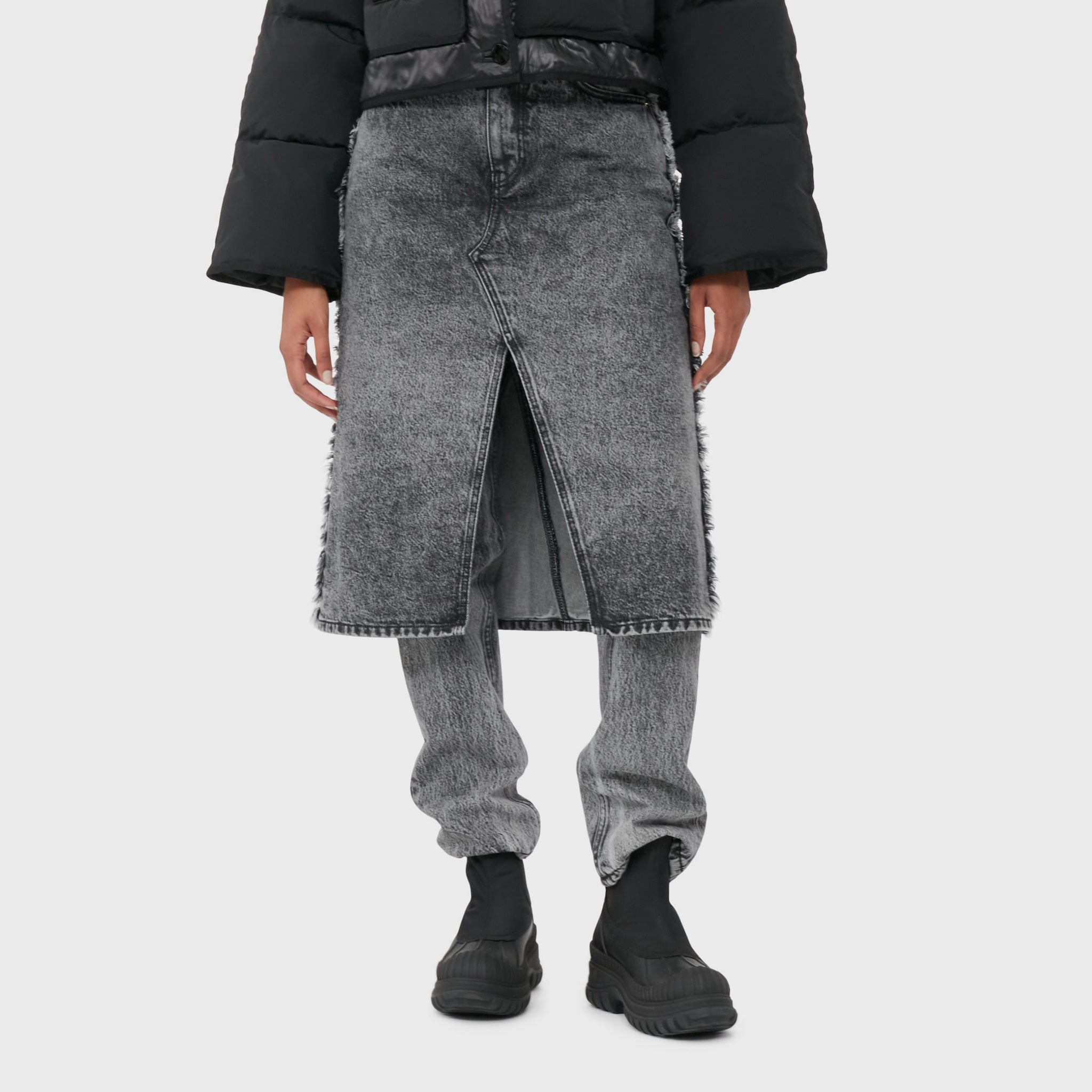 A model wears the acid washed black denim jeans with attached midi skirt with black boots.