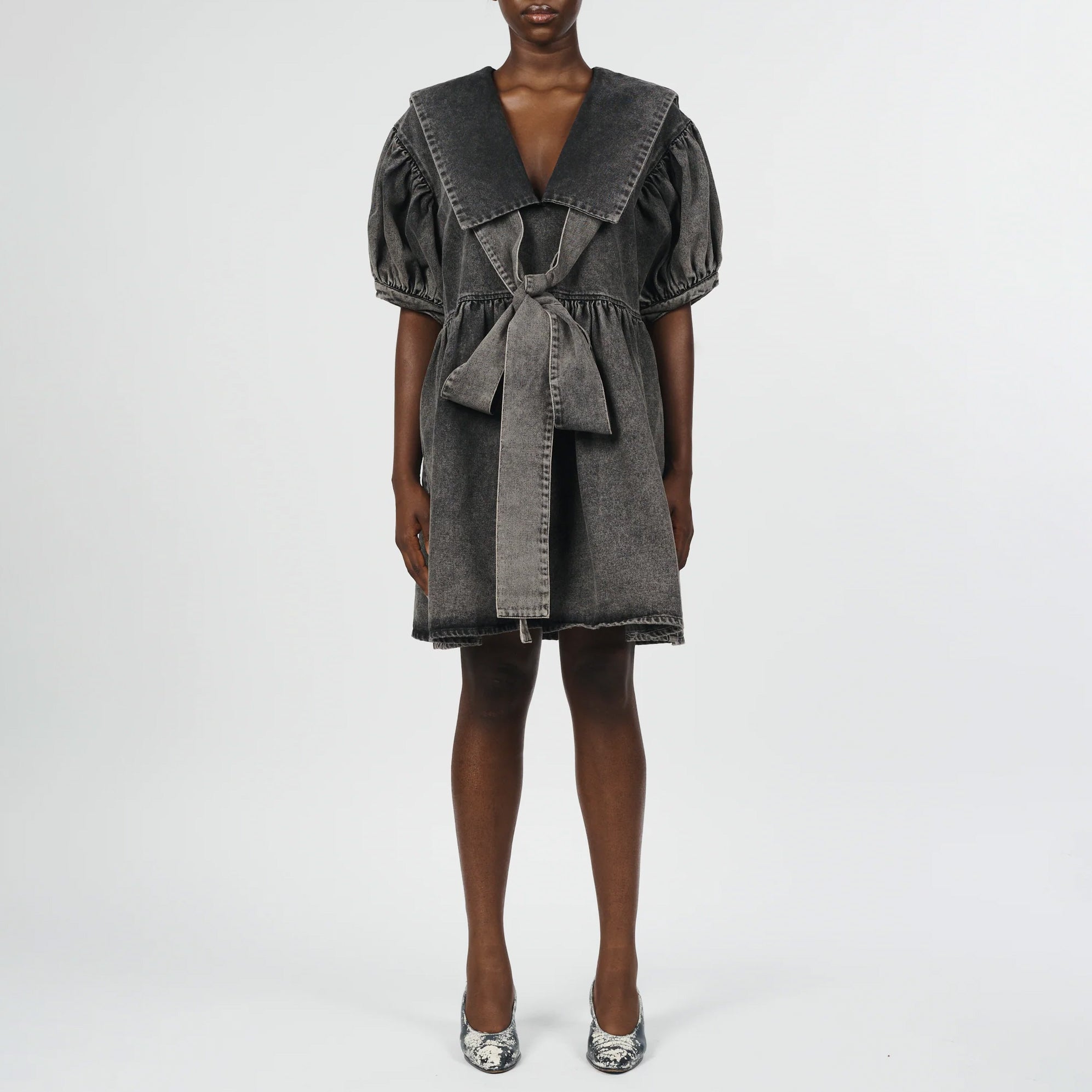 Front full body photo of model wearing a mini black acid wash dress with a large collar and bow detail in the front.