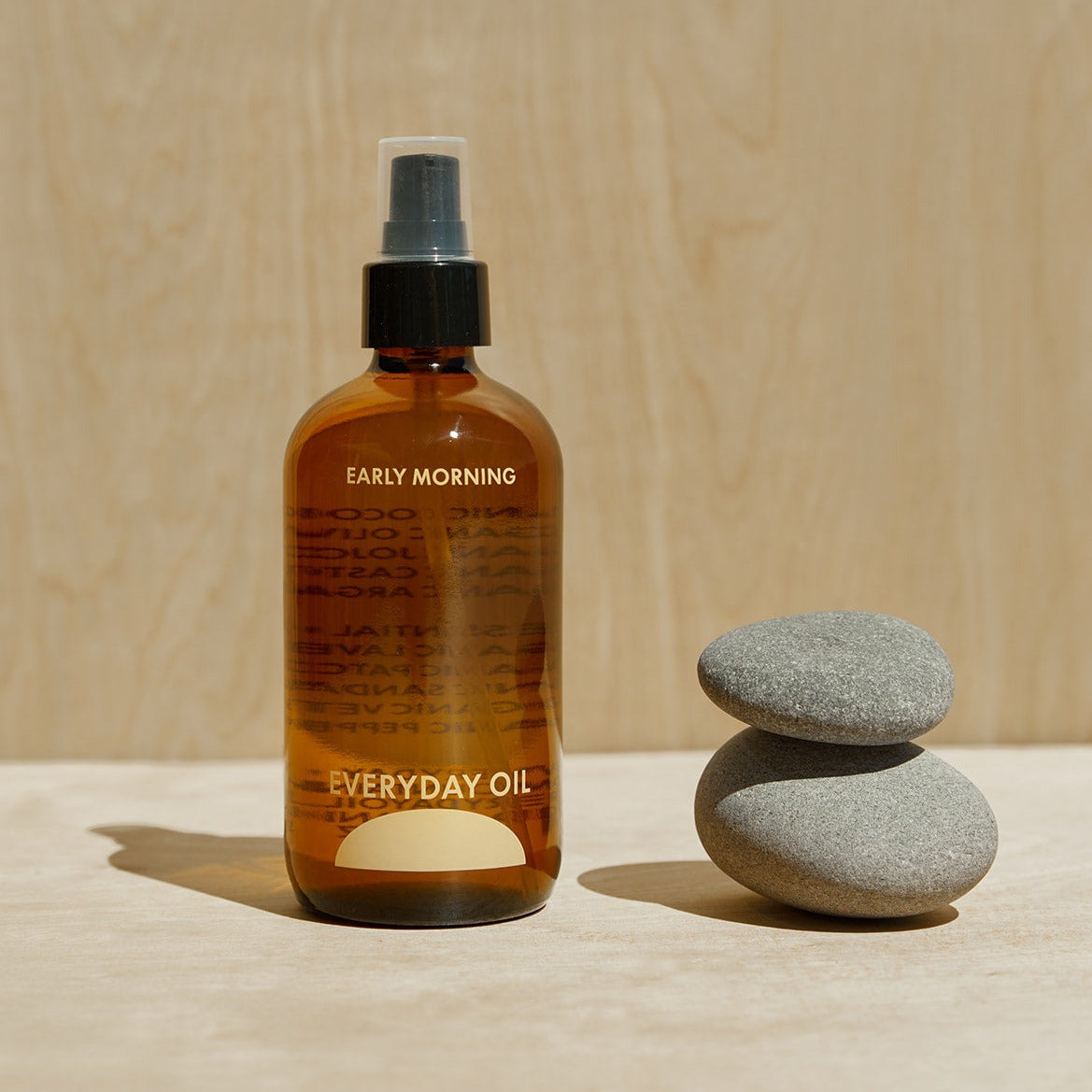 An amber glass bottle labeled EARLY MORNING by Everyday Oil stands on a wood surface next to a couple rocks.