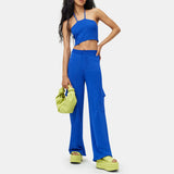 Close detail half body photo of the model wearing the Hesby Pant - a vibrant blue knit wide leg pant with side cargo-style pockets and a button & zip closure - full outfit view.