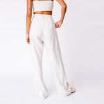 A model wears the high rise linen trousers by Misc Etc, paired with the Tie Top and sneakers, back view.