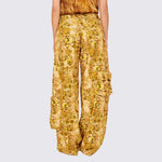 A model wears the gold and brown graphic printed Lawn Cargo Pant featuring various large pockets and a zip fly, back view.