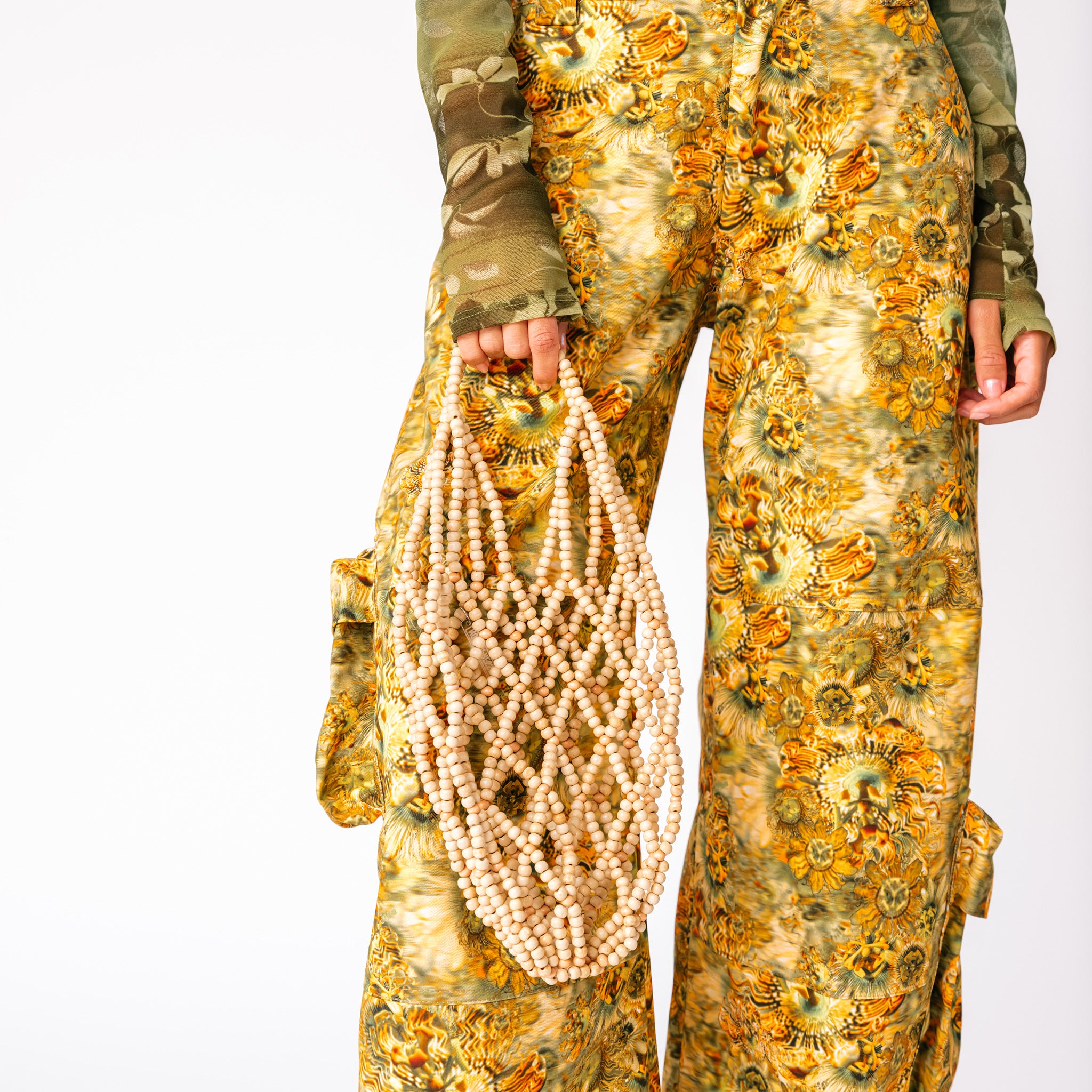 A model wears the brown and yellow floral printed Lawn Cargo Pants by Collina Strada with a mesh green long sleeved top - detail.