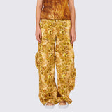 A model wears the gold and brown graphic printed Lawn Cargo Pant featuring various large pockets and a zip fly, front view.