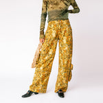 A model wears the brown and yellow floral printed Lawn Cargo Pants by Collina Strada with a mesh green long sleeved top - front view.