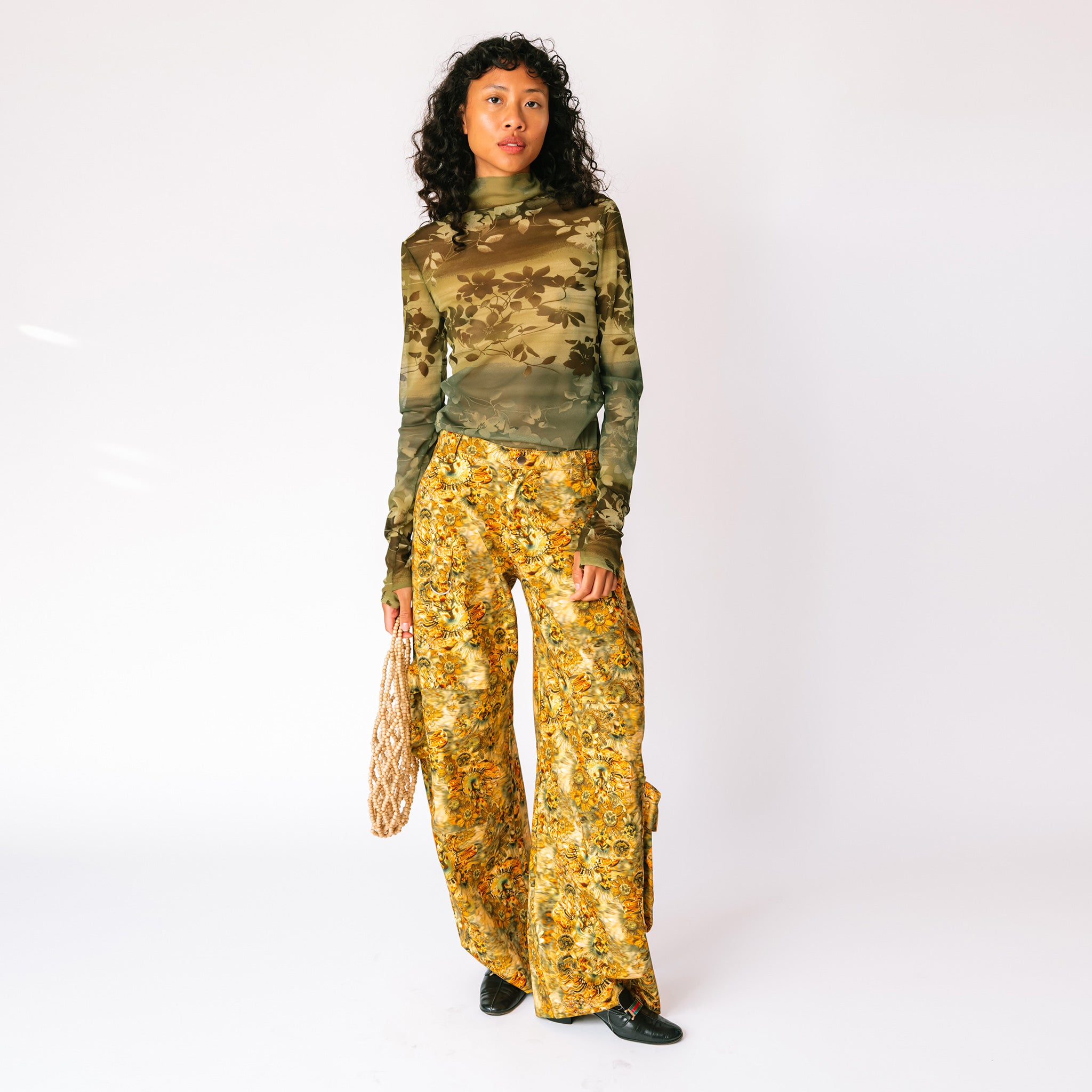 A model wears the brown and yellow floral printed Lawn Cargo Pants by Collina Strada with a mesh green long sleeved top.