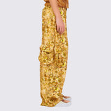 A model wears the gold and brown graphic printed Lawn Cargo Pant featuring various large pockets and a zip fly, side view.