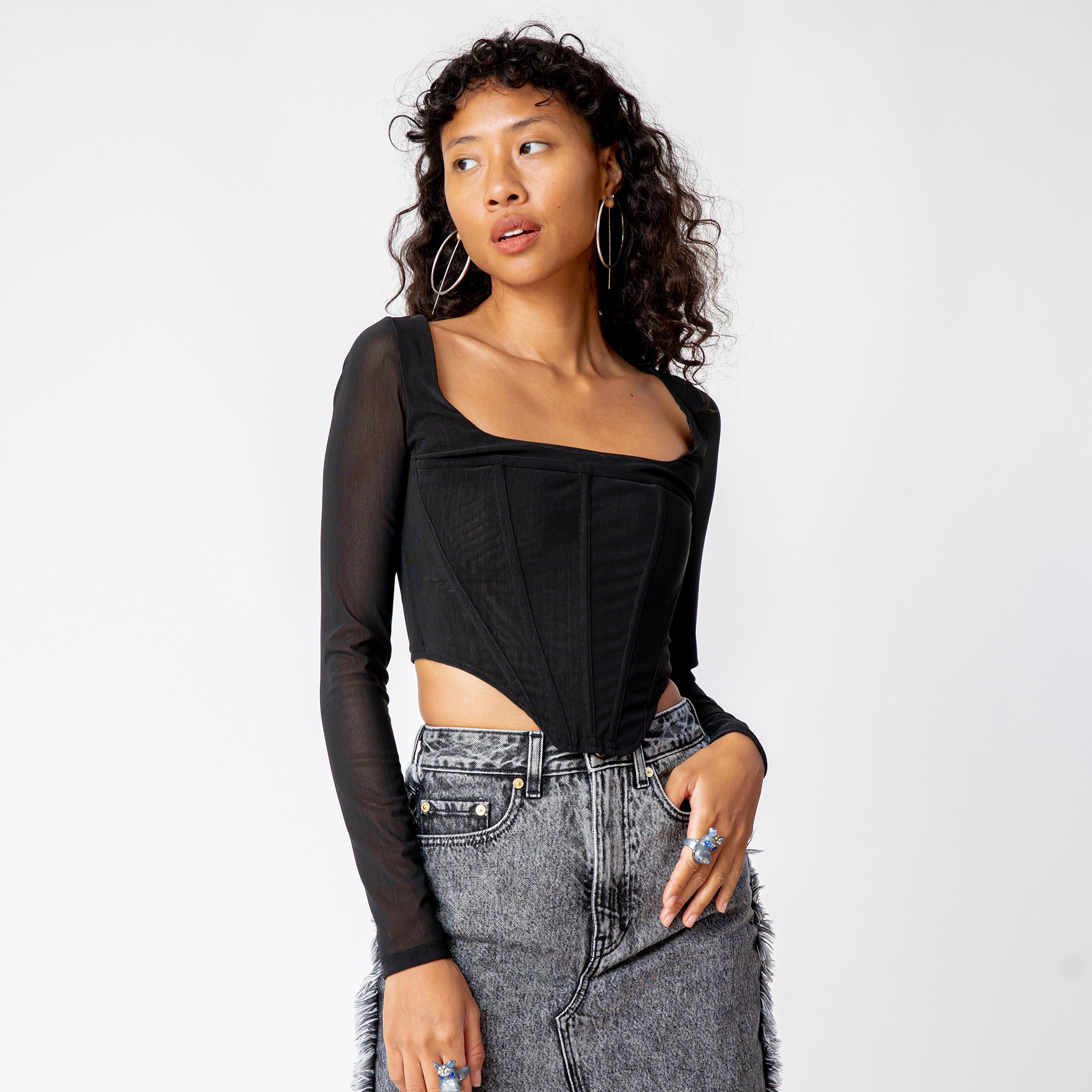A model wears the long sleeved black mesh Maude Corset.