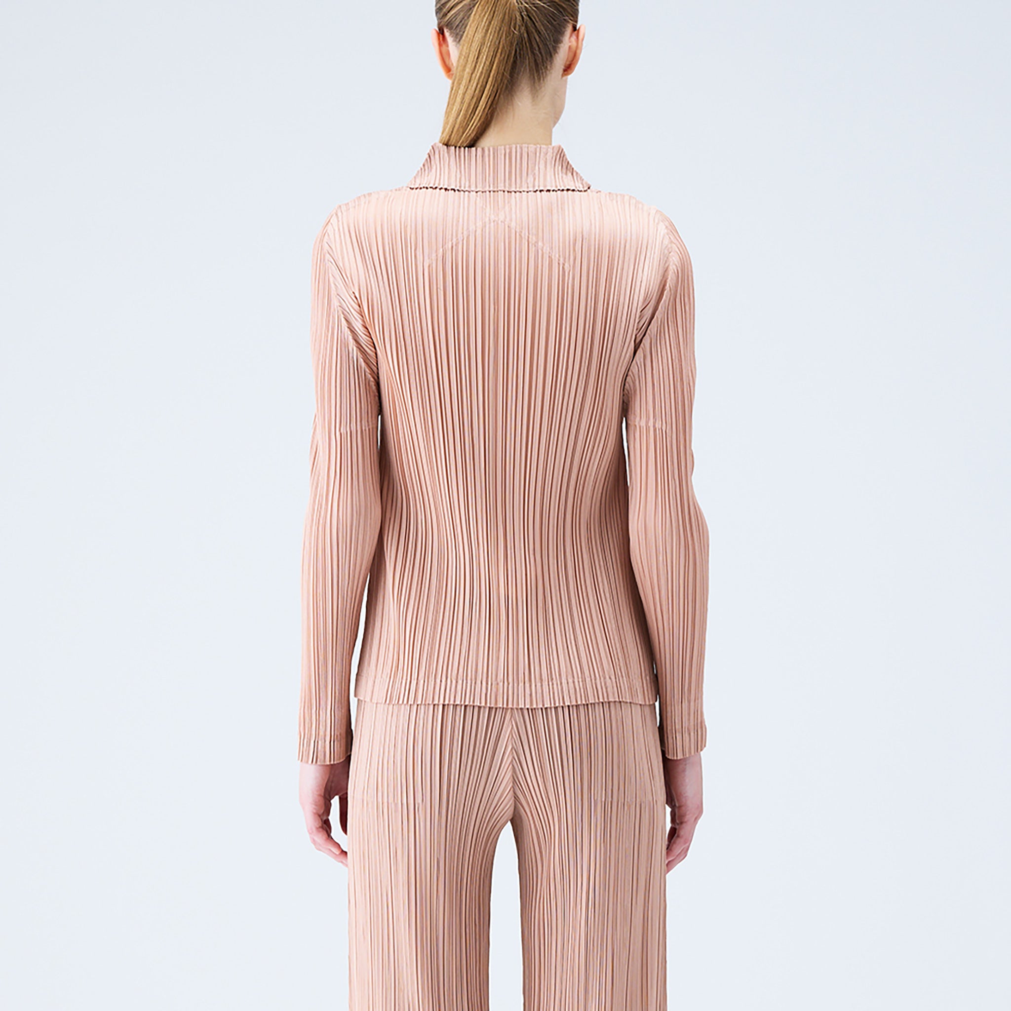 Back half body photo of model wearing the pleated polo top in the color beige.
