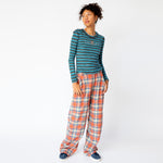 Full outfit view of the blue and brown striped Cardio Crew by Collina Strada featuring rhinestones on the chest in the shape of a teddy bear and swirls, paired with orange and white plaid wide leg pants..