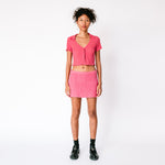 A model wears Misc Etc's pink ruched polo top in dark rose, paired with a matching pink mini skirt and black loafers, full outfit view.