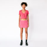 A model wears Misc Etc's pink ruched polo top in dark rose, paired with a matching pink mini skirt and black loafers, full outfit view.