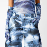 A model wears the blue and white graphic dolphin printed, wide leg Stomp Pant by Collina Strada with matching mesh top and gloves - detailed close up.