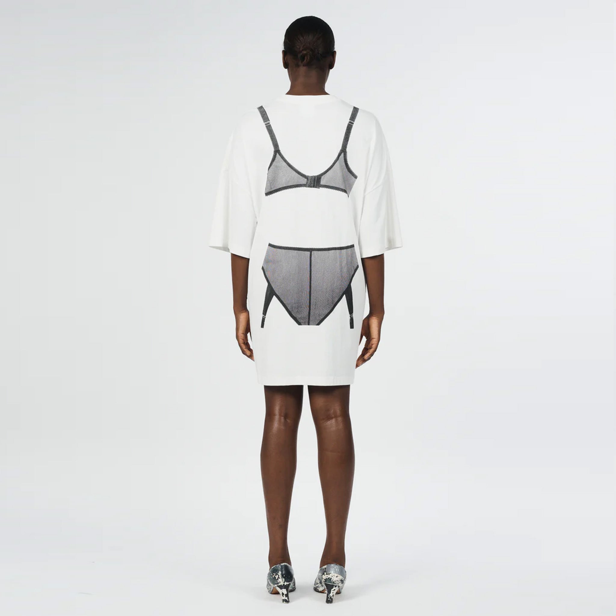 Back full body photo of model wearing the oversized white t shirt with a black graphic printed on the back.