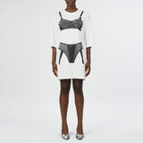 Front full body photo of model wearing a oversized white t shirt with a black bra and underwear graphic detail on the front.