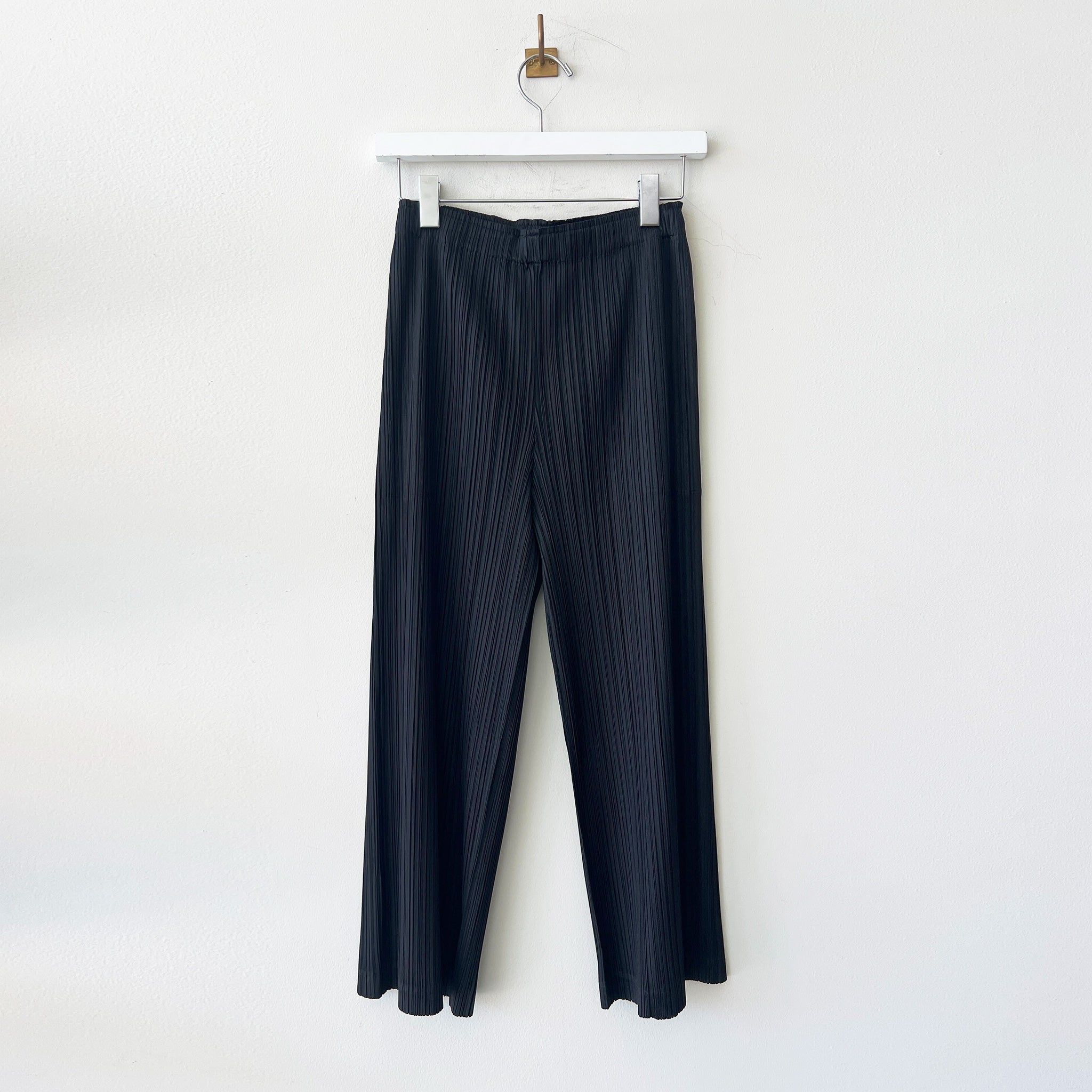 Hanger photo of black Pleats Please pants with a full straight leg, thicker pleating, and hidden side pockets.