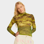 A model has her hand on her hips and wears the green floral mesh Thumbtastic top by Collina Strada.