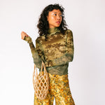 A model wears the long sleeved mesh Thumbtastic Top in an ombre green print with floral and leaves silhouettes - front view.