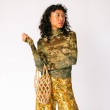 A model wears the long sleeved mesh Thumbtastic Top in an ombre green print with floral and leaves silhouettes - front view.