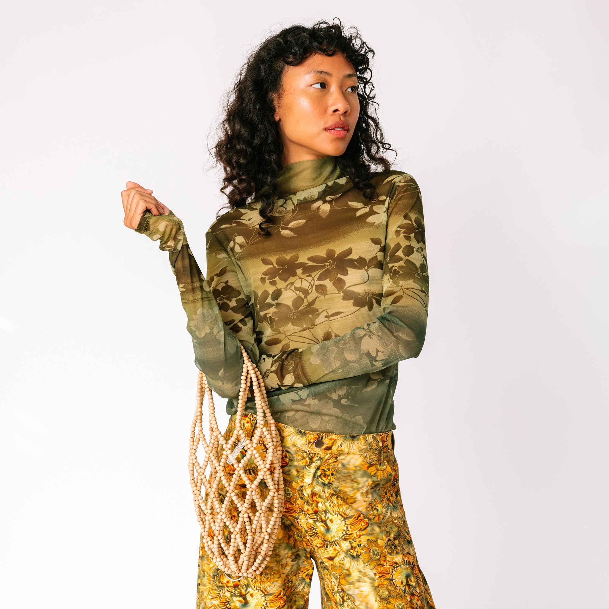 A model wears the long sleeved mesh Thumbtastic Top in an ombre green print with floral and leaves silhouettes - front view.