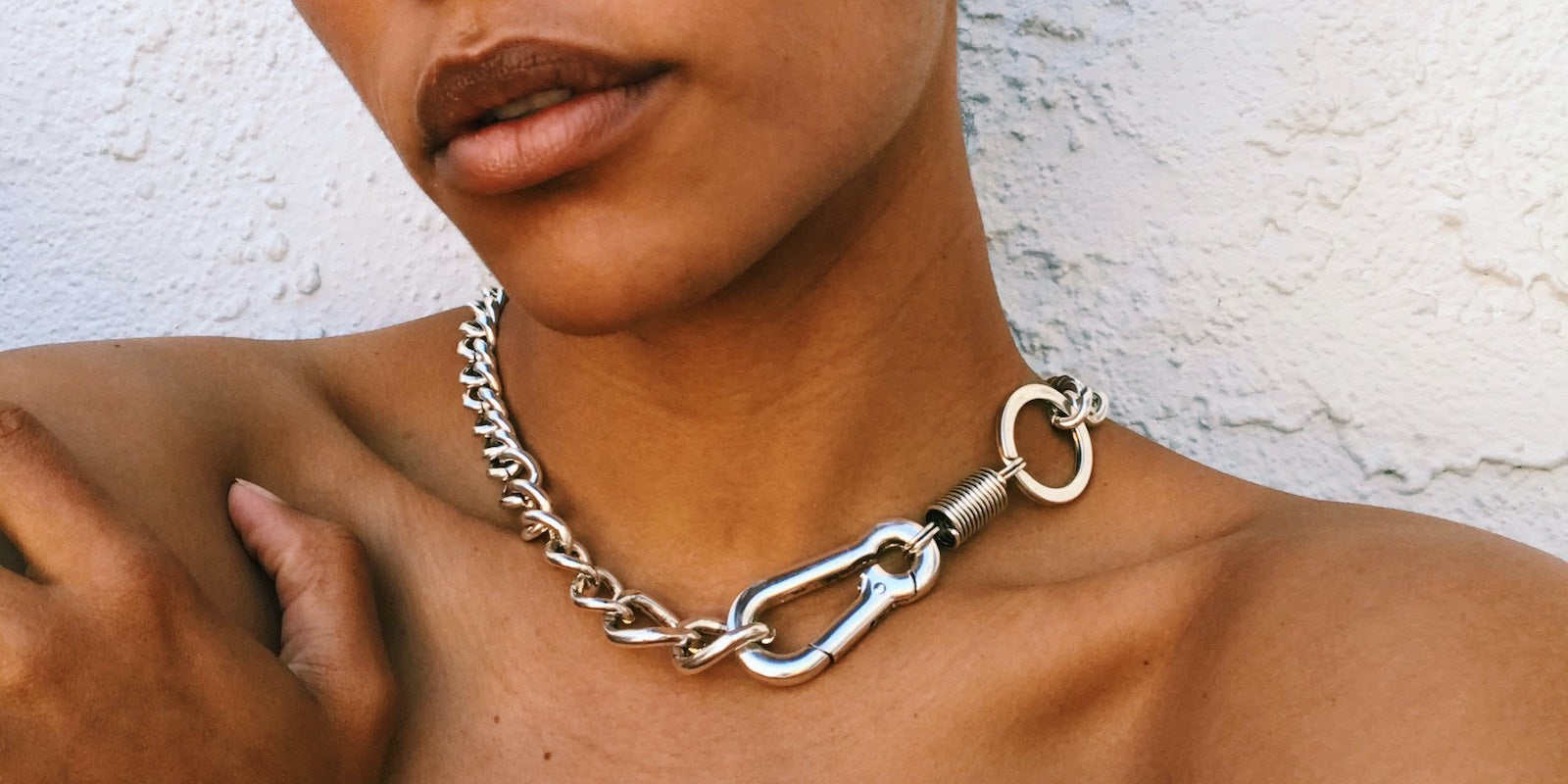 Close up of Courtney wearing a silver chain necklace against a white wall.