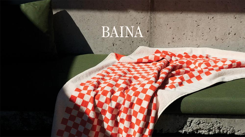 A red and white checked Baina pool towel is thrown against an outdoor bench.