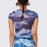 A model wears the blue and white graphic printed mesh Arc top, with ruching details along the chest and shoulders, back view.