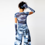 A model wears the blue and white printed mesh Arc Top by Collina Strada with matching cargo pants and gloves - back view.