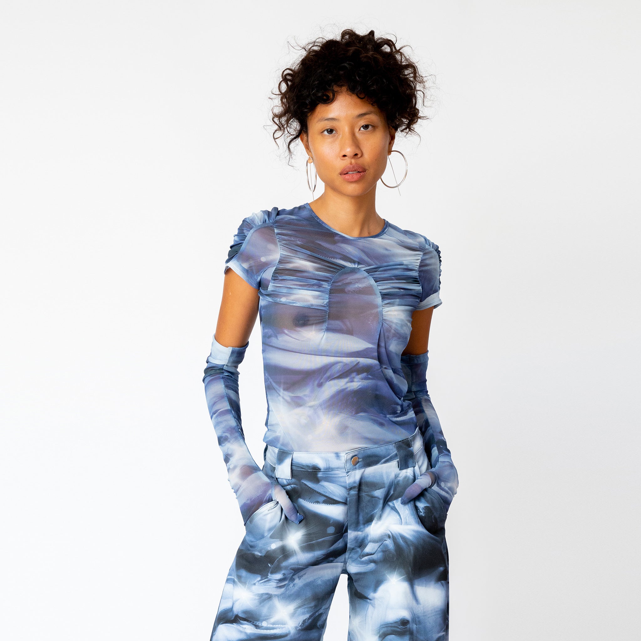 A model wears the blue and white printed mesh Arc Top by Collina Strada with matching cargo pants and gloves.