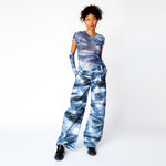 A model wears the blue and white printed mesh Arc Top by Collina Strada with matching cargo pants and gloves.