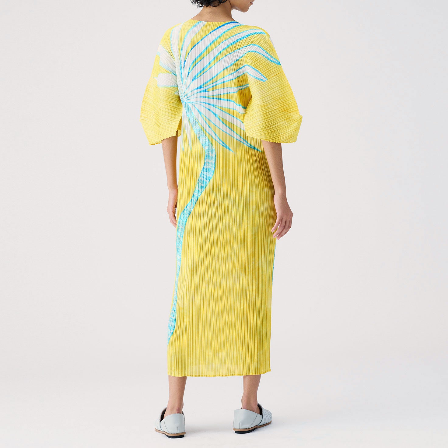 Back view of the full length pleated dress in yellow with exaggerated sleeves.