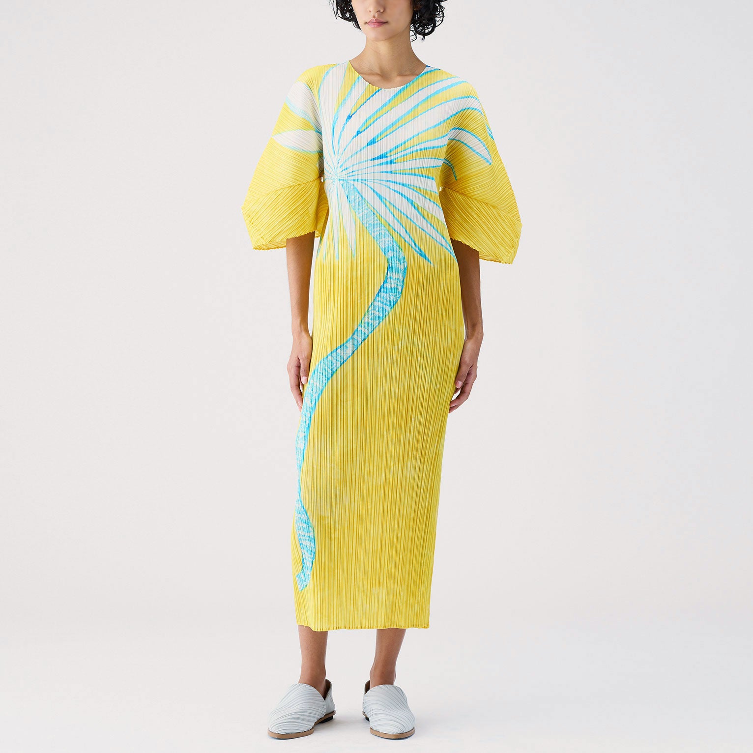 Full length yellow pleated dress with exaggerated 3/4 length sleeves and ice blue graphic if spindly plant.