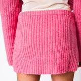 A model wears the Barb chunky ribbed pink skirt with the matching chunky ribbed pink Paw Cardigan, back view.