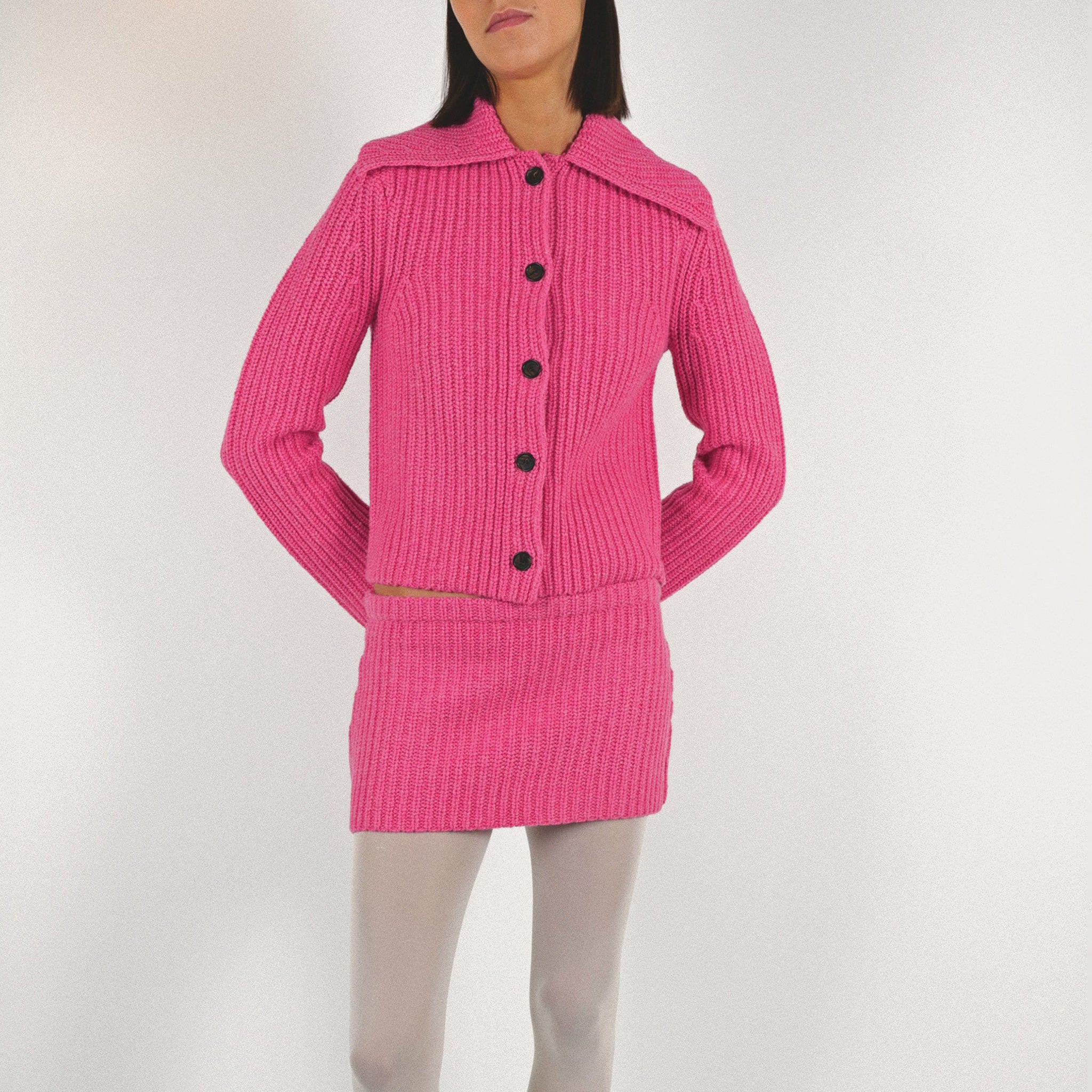 Close half body photo of model wearing a pink mini knit skirt paired with a pink knit sweater.