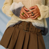 A model wears the Misc Etc belted pleated mini skirt in khaki, paired with a pale yellow sweater, close up view.
