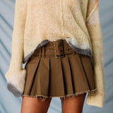 A model wears the Misc Etc belted pleated mini skirt in khaki, paired with a pale yellow sweater, leg warmers, close up of belt.
