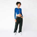 A model looks to the side while wearing the Big Ol' Jeans in washed black canvas in a baggy fit, paired with a cropped blue sweater and white sneakers.