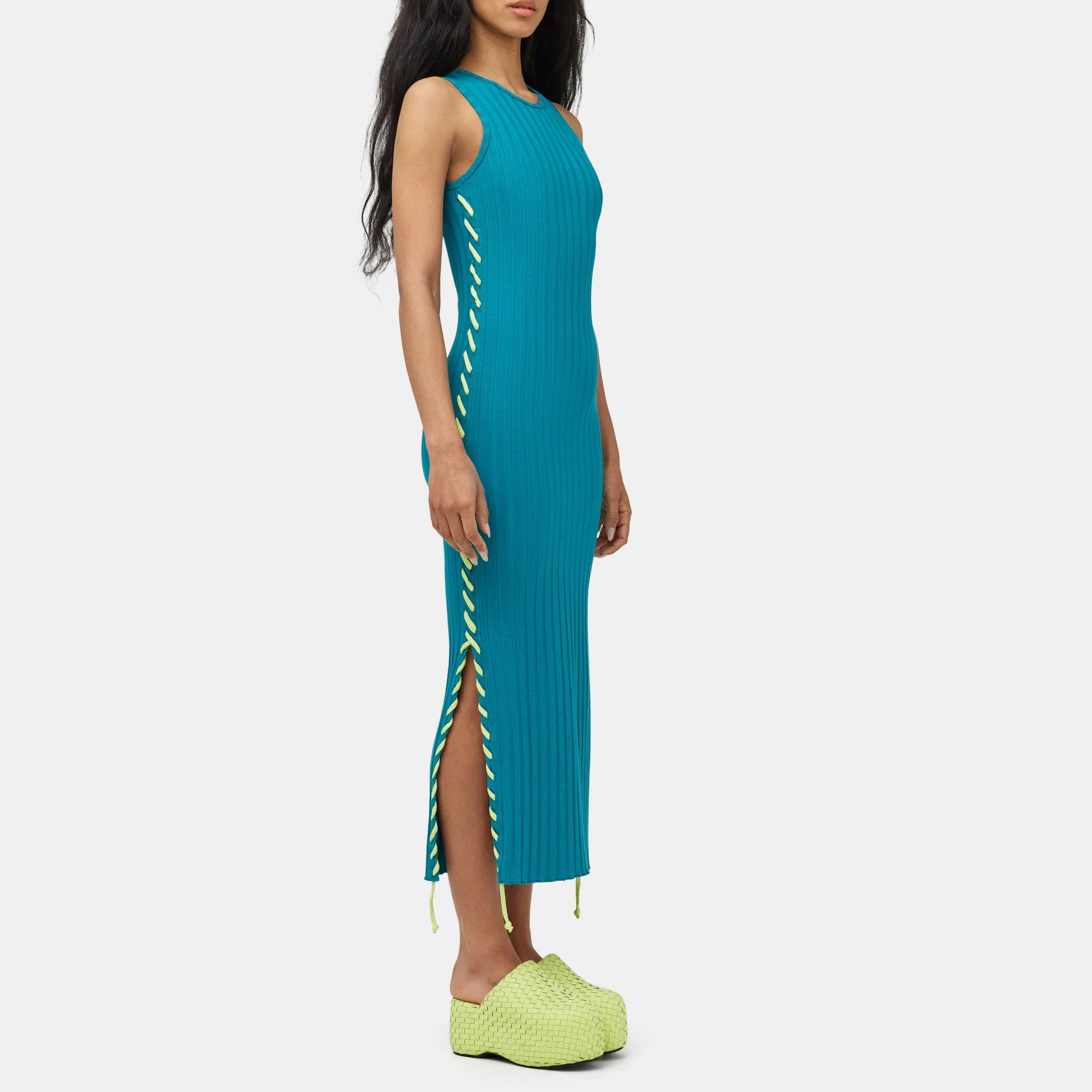 Full body photo of model wearing the teal green ribbed Blix Dress, a sleeveless ribbed dress with fluorescent green oversized stitching detail along the sides.