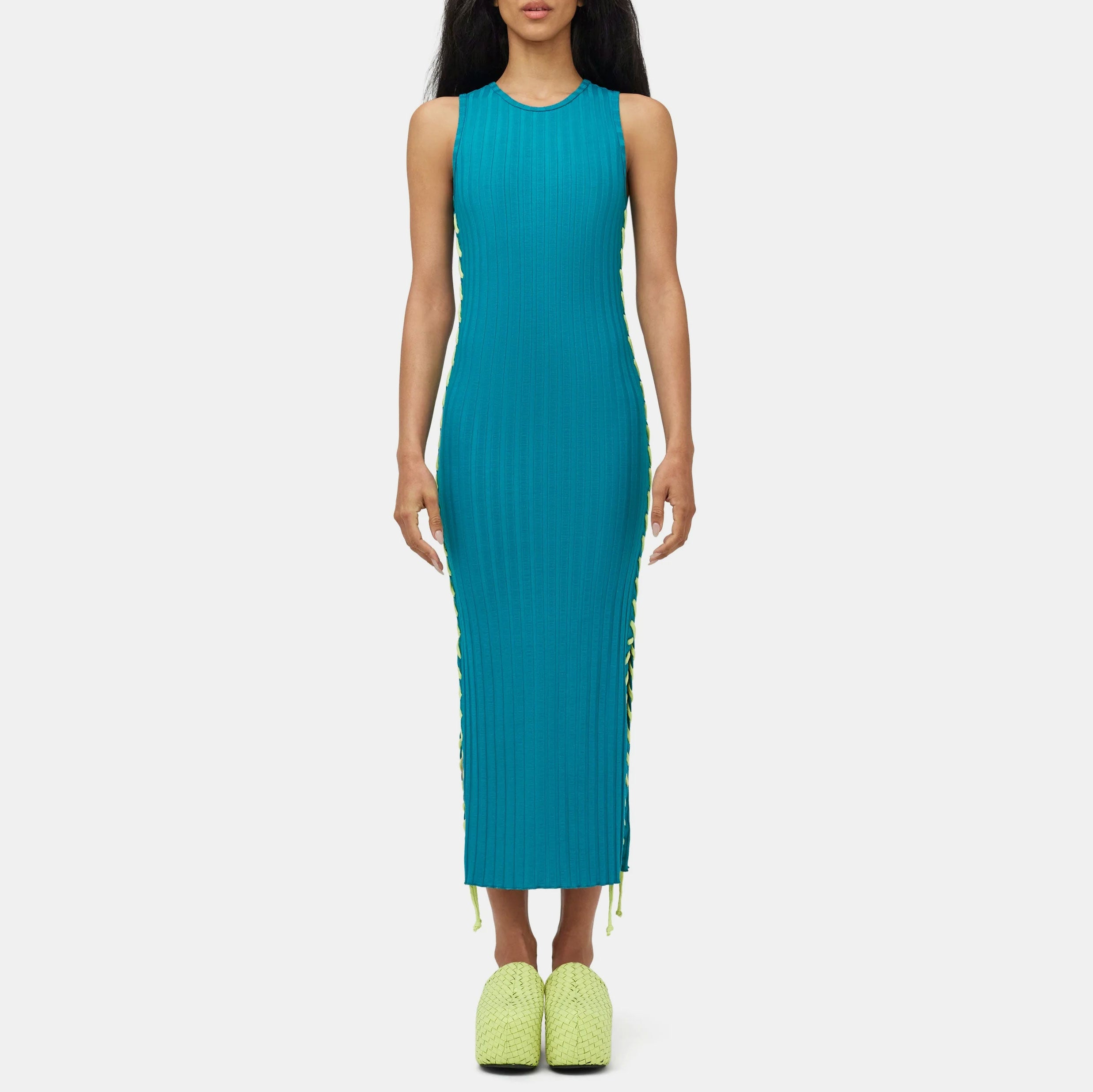 Full body photo of model wearing the teal green ribbed Blix Dress, a sleeveless ribbed dress with fluorescent green oversized stitching detail along the sides - front view.
