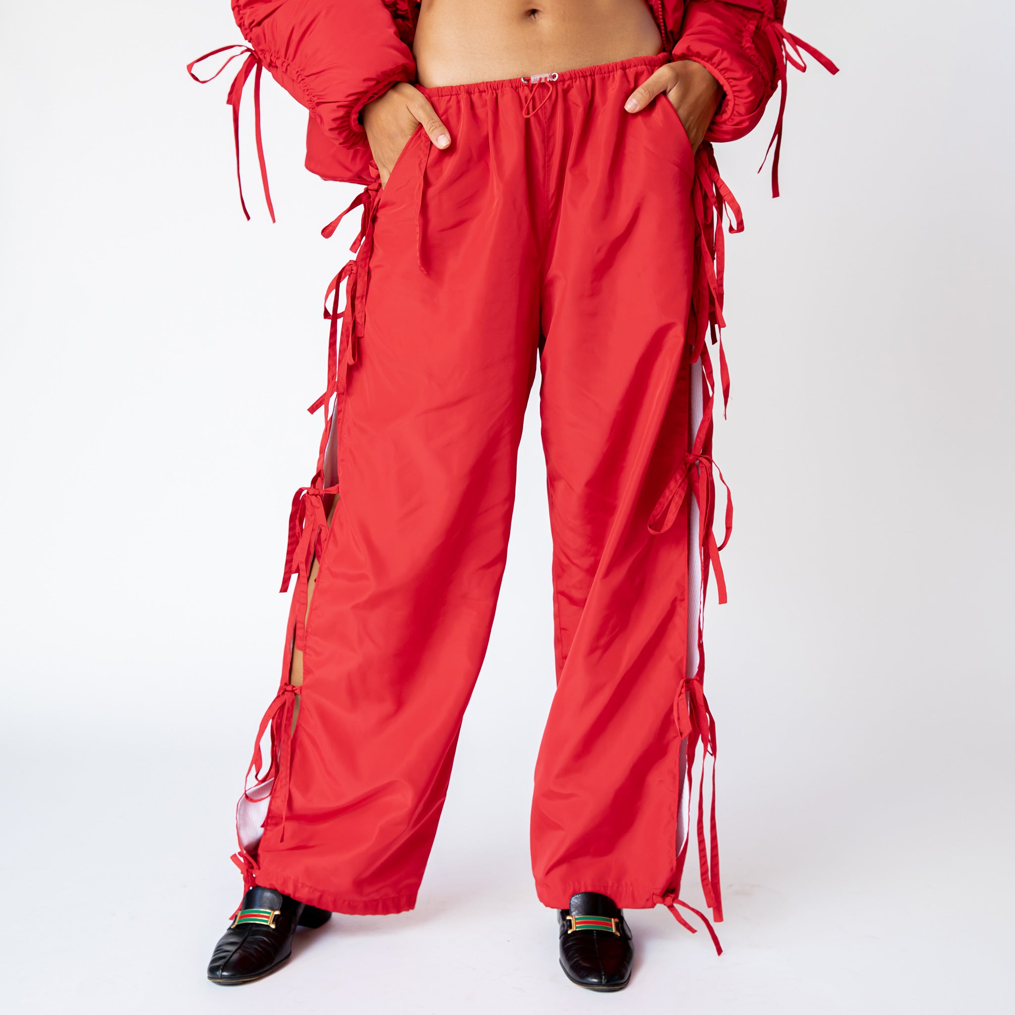 Front half body photo of model wearing the Cam Pants in the color red with bow details down the side.
