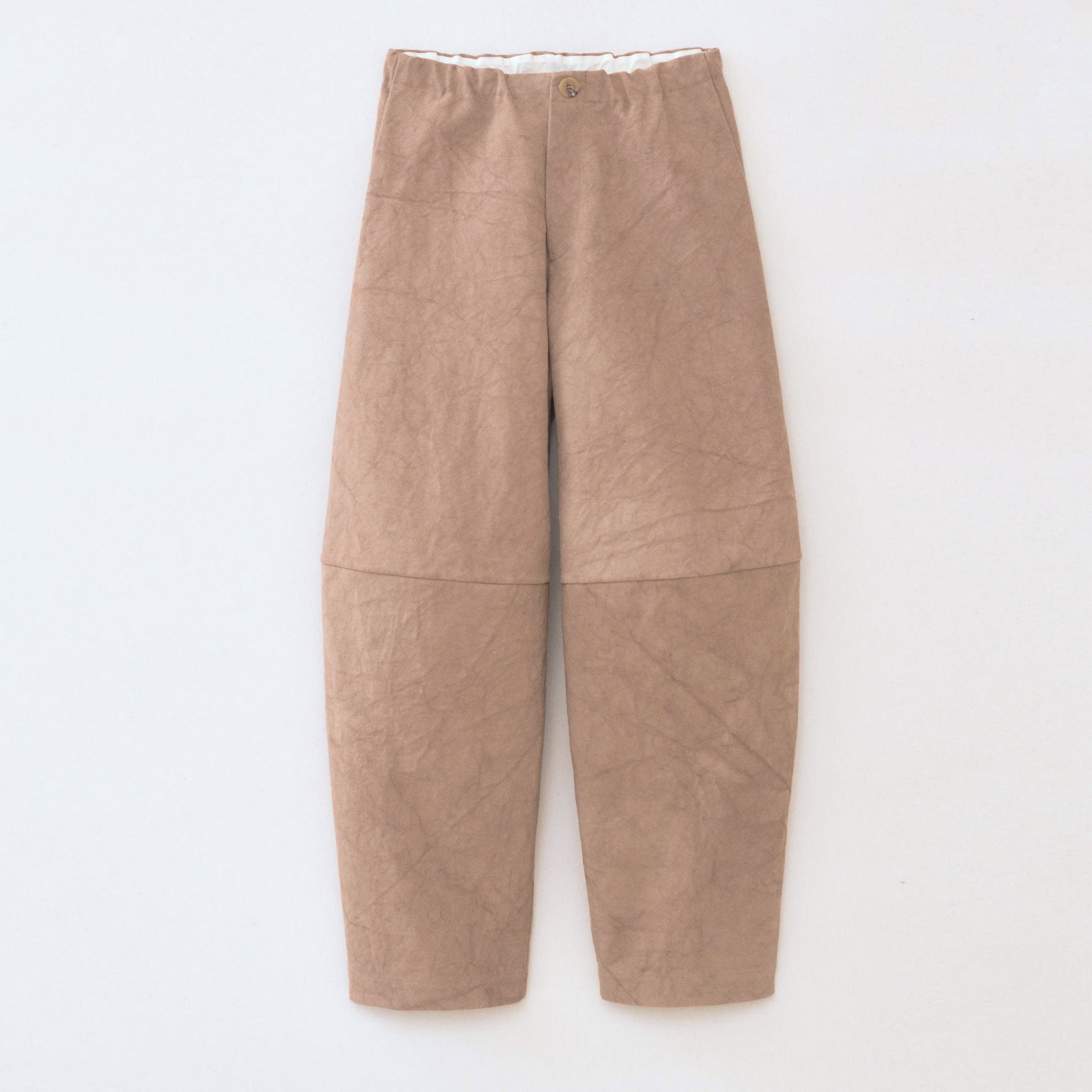 A model wears the Canvas Pants in a light brown color with a slightly rumpled and naturally dyed effect, side pockets, and a partial elastic waistband, flat view.