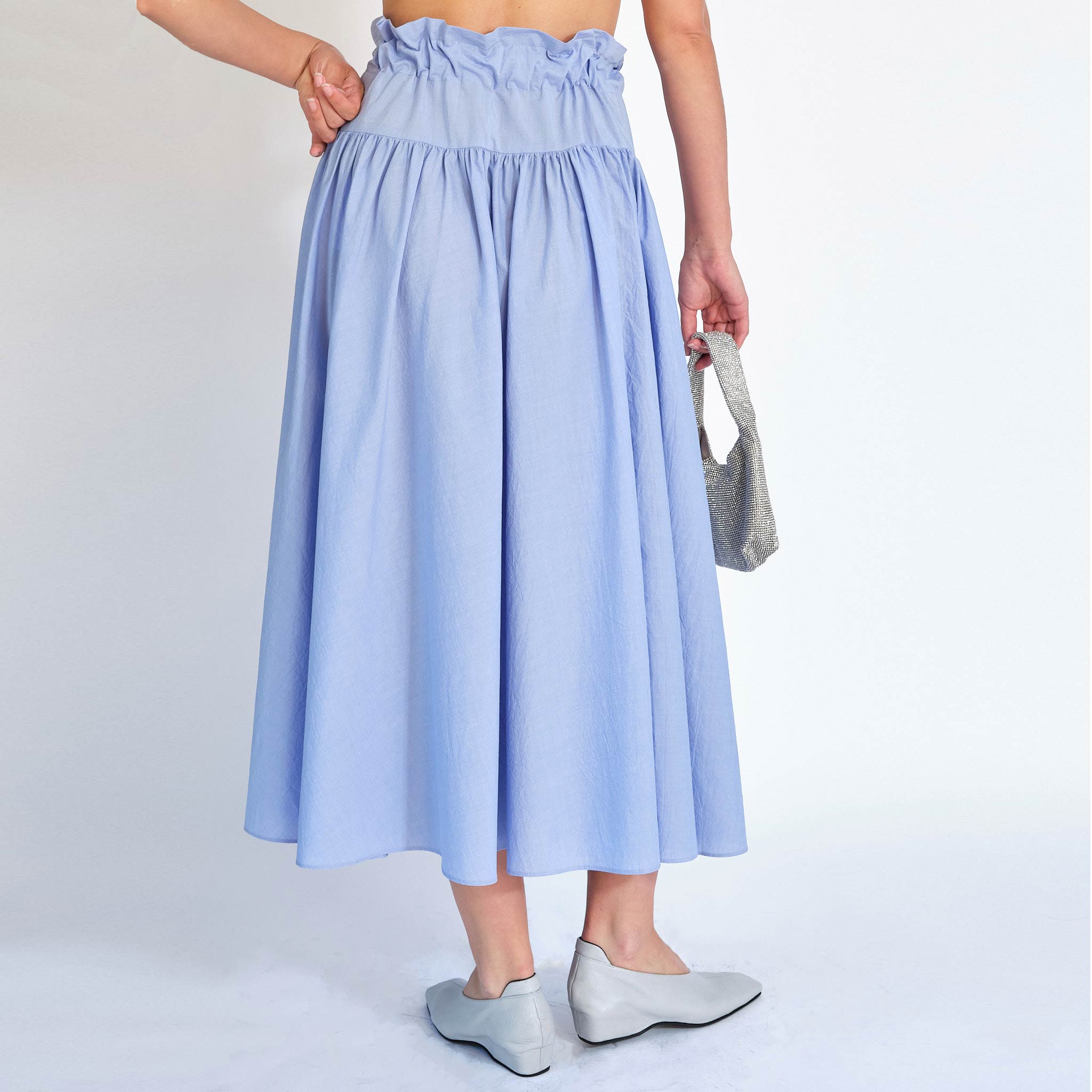 A model wears the Carlita Skirt, with a ruched, paperbag style waist and built in tie, with a side slit opening - back view.