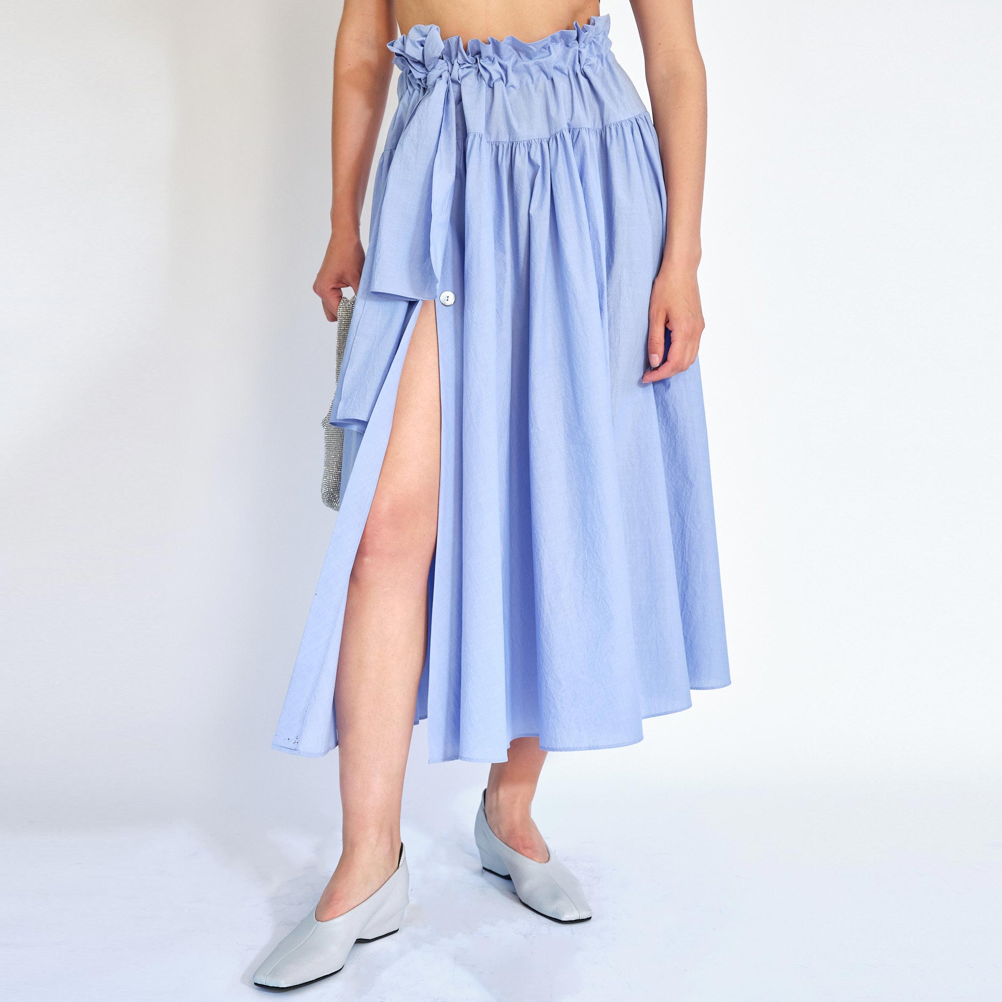A model wears the Carlita Skirt, with a ruched, paperbag style waist and built in tie, with a side slit opening - front view.
