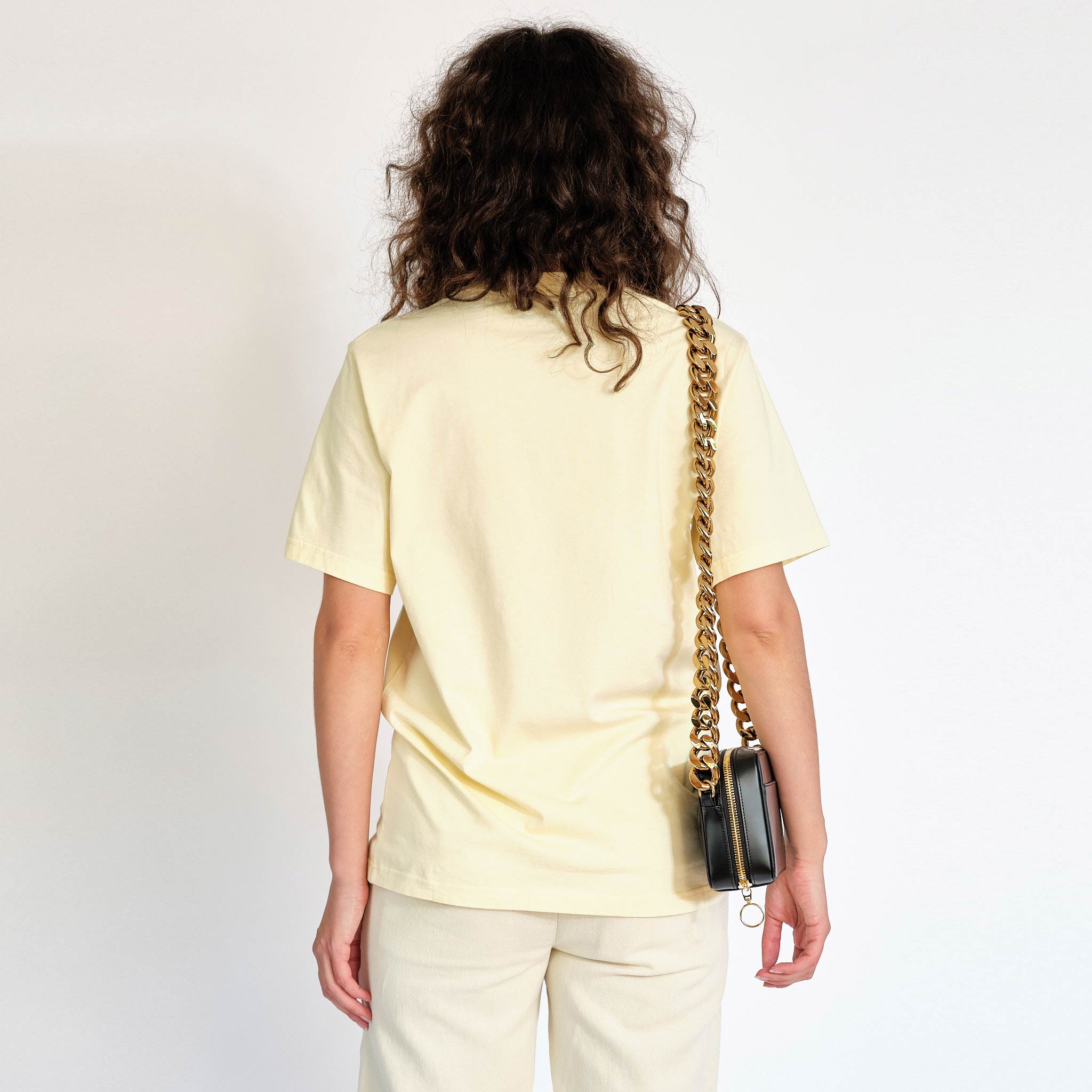 A model wears the light yellow Martine Rose t-shirt featuring a sock puppet graphic and the words Eager Beaver on the front chest - back view.