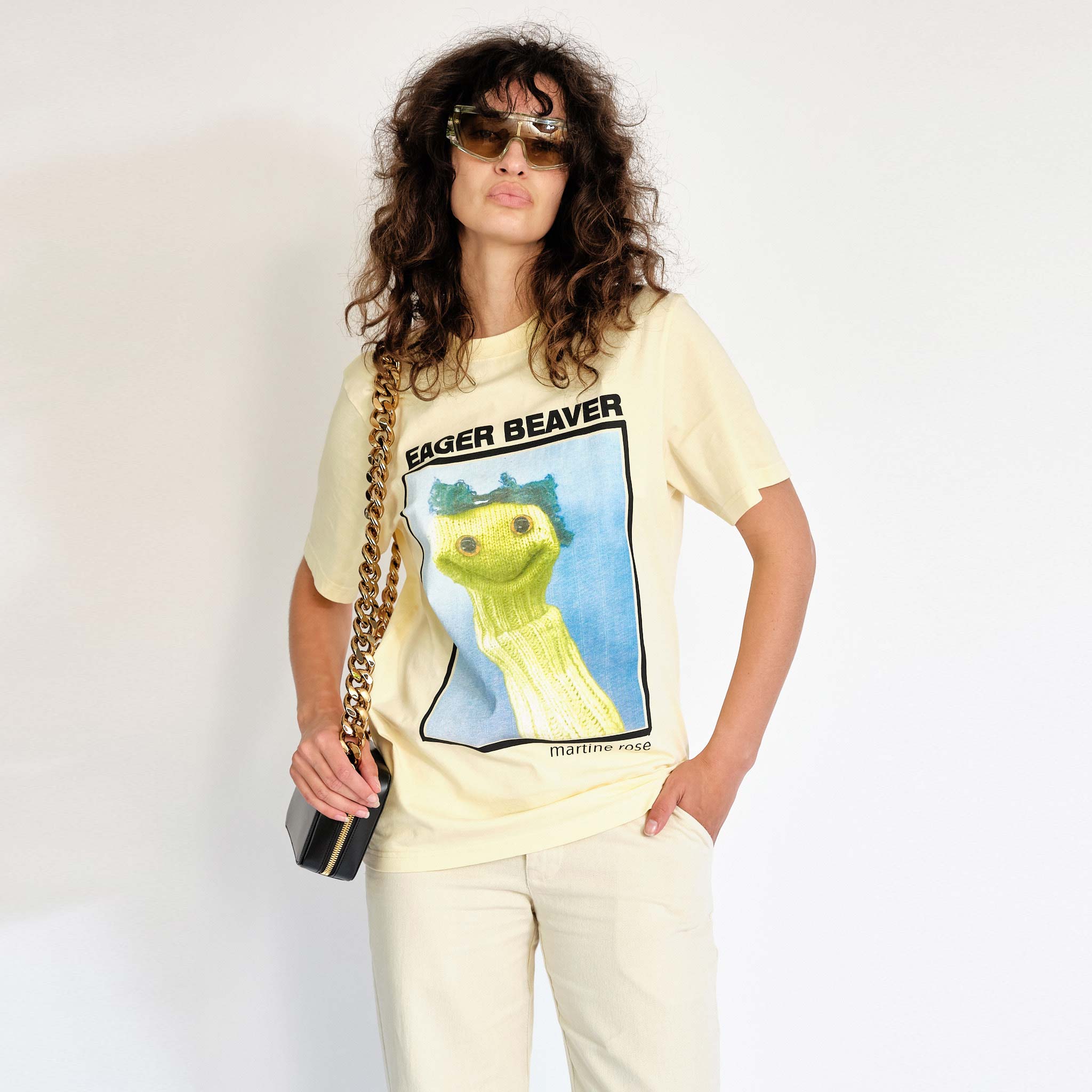 A model wears the light yellow Martine Rose t-shirt featuring a sock puppet graphic and the words Eager Beaver on the front chest - front view.